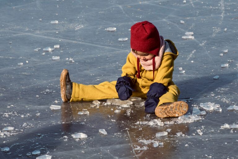 child in yellow jacket and red knit cap playing on water